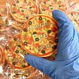 Hand met blauwe handschoen decoreert pizza-koekje voor kindertraktatie