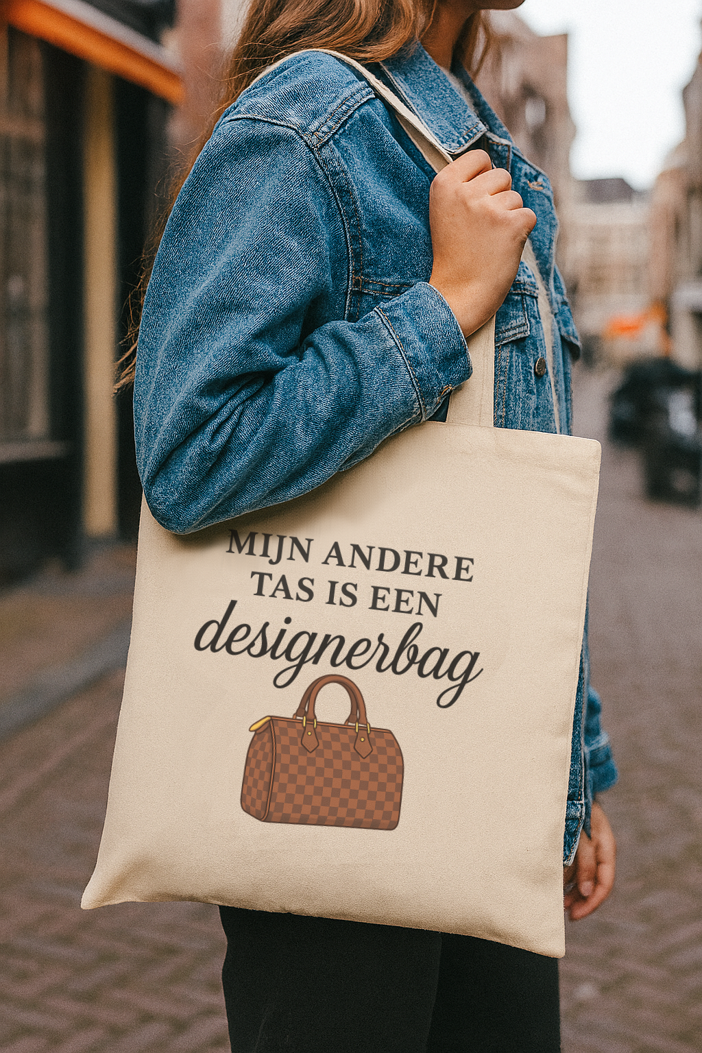 Vrouw draagt een katoenen tote bag met de tekst ‘Mijn andere tas is een designerbag’ in een stadse omgeving