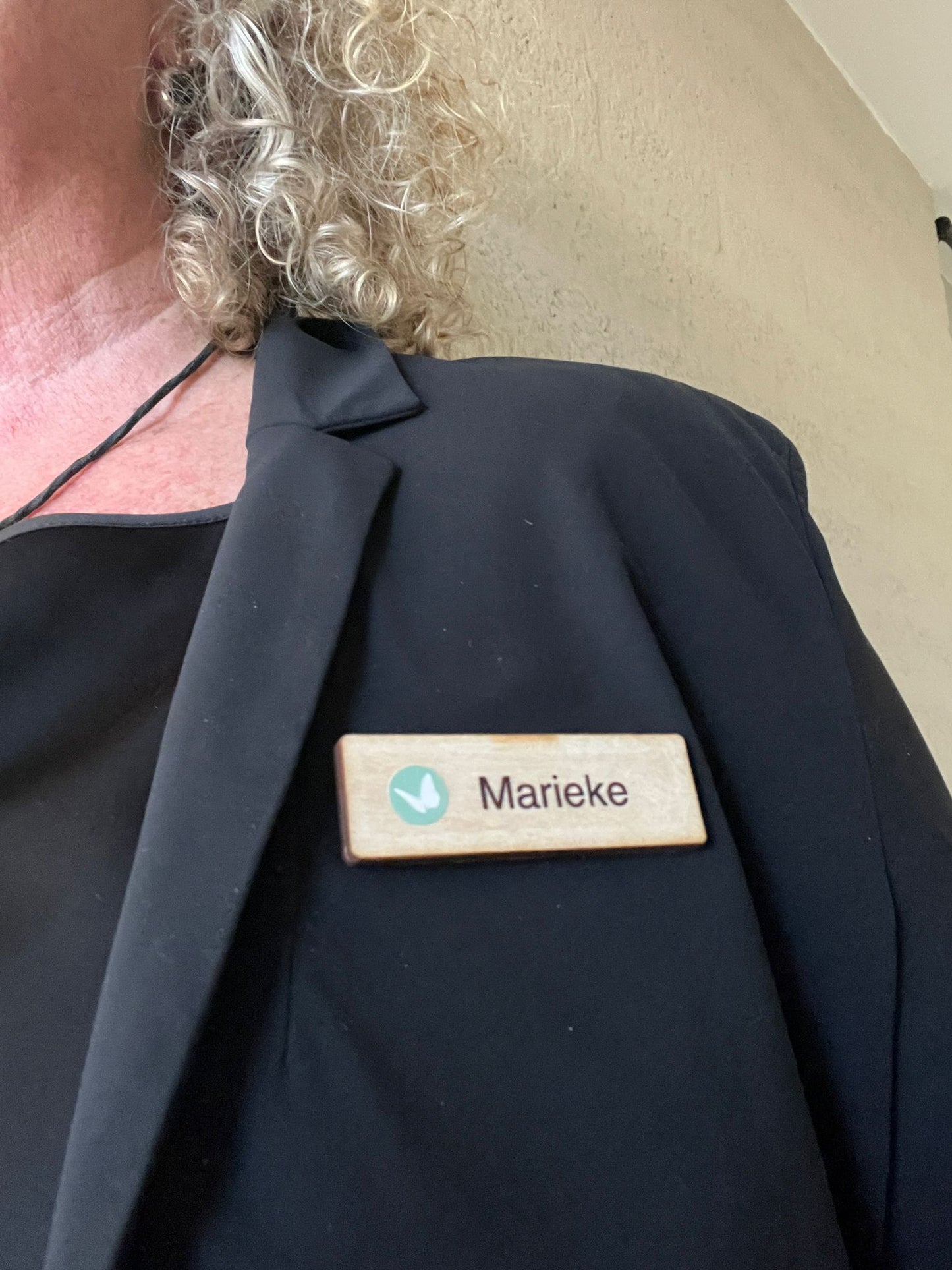 Houten badge met naam Marieke en vlinder logo, gedragen op een donkere jas met magneetsluiting