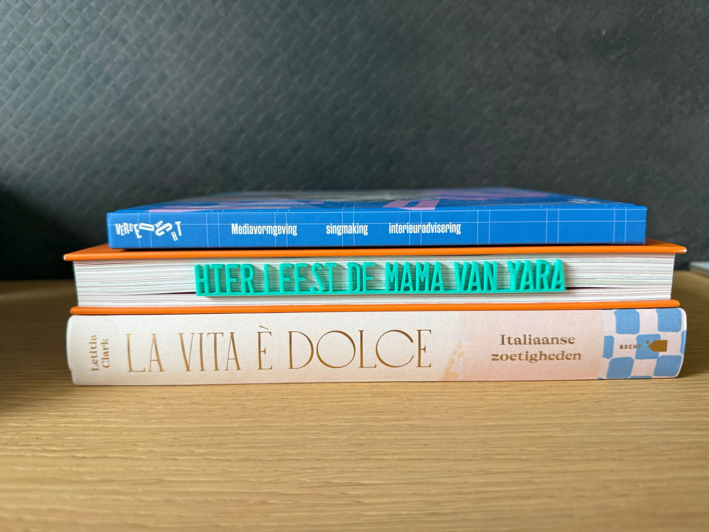 Turquoise 3D geprinte boekenlegger met de gepersonaliseerde tekst 'Hier leest de mama van Yara' tussen een stapel boeken. Gemaakt door Traktatiecorner in Venlo.